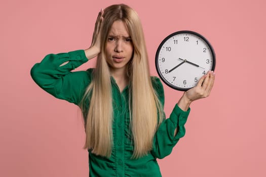 Confused woman with anxiety checking time on clock, running late to work, being in delay, deadline