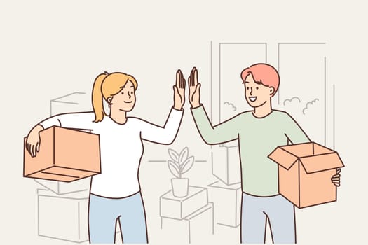 Happy married couple moving into new house and giving each other high five standing with boxes
