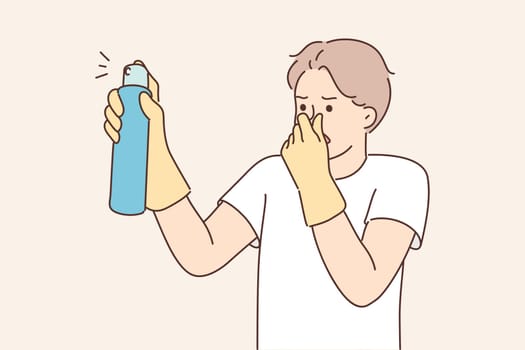 Dissatisfied man with spray to remove unpleasant odors covers nose with hand spraying freshener