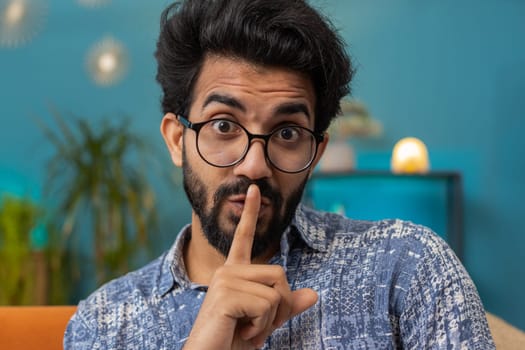 Indian man presses finger to lips makes silence hush sign do not tells gossip secret, quiet at home