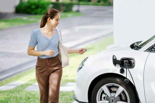 Progressive woman recharge her EV car at home charging station.