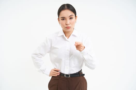 Portrait of businesswoman with strict, serious face expression, points finger at camera, teaches a lesson, white studio background