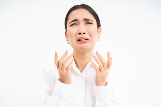 Upset asian woman looks up with desperate and sad face, complains to Lord, stands over white background