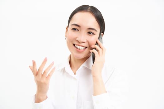 Portrait of asian corporate woman, businesswoman talks on mobile phone, has conversation over cellphone, speaking on telephone, white background