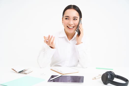 Image of office employee, asian woman in office talks on mobile phone, discusses work on cellphone, white background