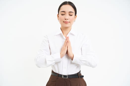 Smiling calm young woman, holds hands in pray with eyes closed, makes wish, hopes for smth, white background