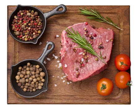 Raw piece of beef with spices pepper, rosemary sprig, salt and olive oil on a wooden board