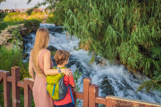 Mother and son tourists on the background of Duden waterfall in Antalya. Famous places of Turkey. Lower Duden Falls drop off a rocky cliff falling from about 40 m into the Mediterranean Sea in amazing water clouds. Tourism and travel destination photo in Antalya, Turkey. Turkiye