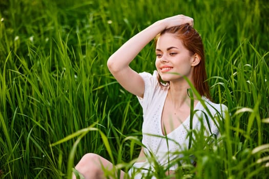 cute woman with red hair sits in tall green grass with her hand on her head