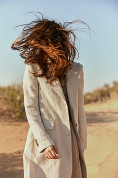 portrait of a woman in a light jacket with hair covering her face from the wind
