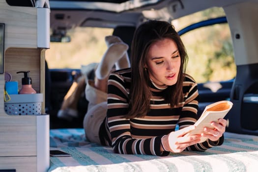 young woman relaxing in camper van reading book