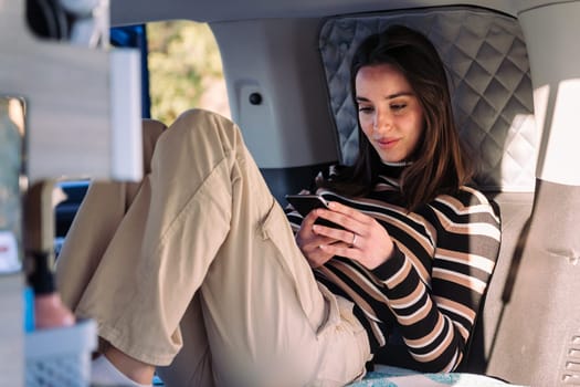 young woman relaxing in camper van using phone