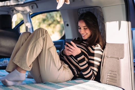 smiling woman relaxing in camper van using phone