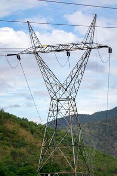 Image of high voltage electricity pylon and transmission power line with sky and mountain background.