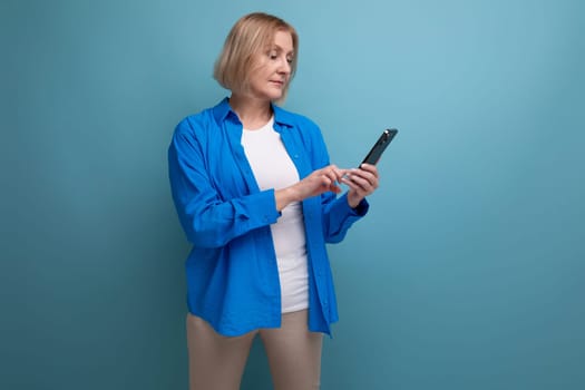blond mature woman with bob haircut communicates by smartphone on studio background