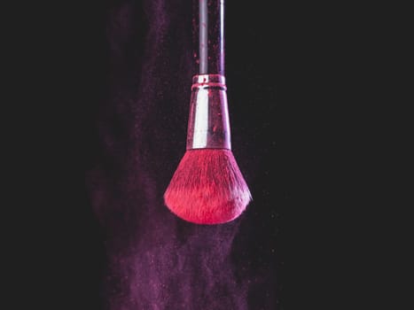 Make-up brush with pink powder splashes explosion on black background. Beauty concept