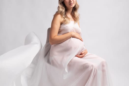 Close up elegant pregnant young woman standing wearing flying white fabric. Pregnancy, maternity and motherhood concept.