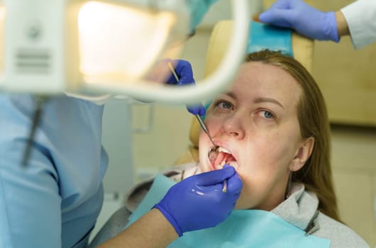 A doctor examines a woman's teeth with a dental instrument.
