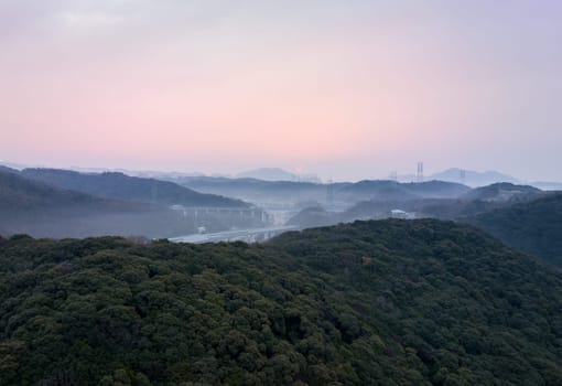 Sun rises on horizon and highway through misty mountain valley