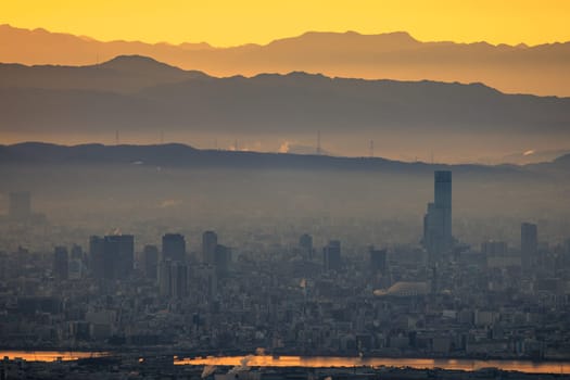 Haze layer over city by river and mountains with orange sunrise glow