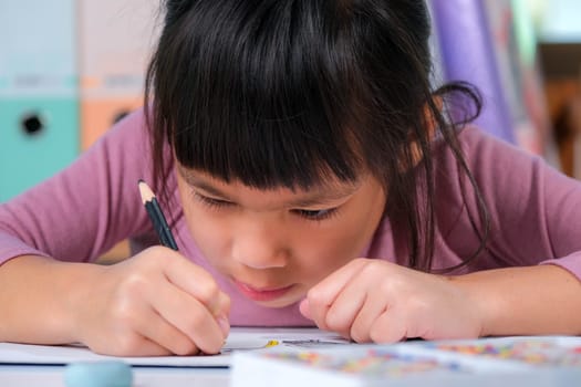 Happy little girl drawing with colored pencils on paper sitting at table in her room at home. Creativity and development of fine motor skills.