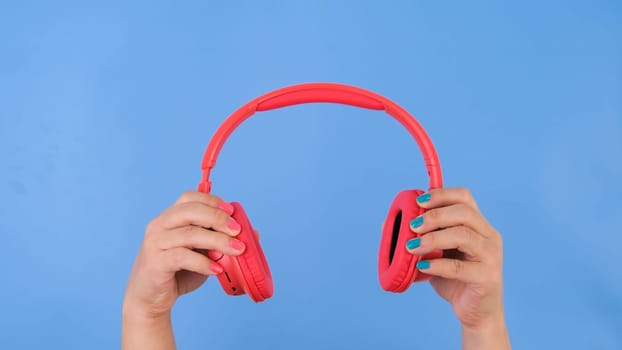 Female hands holding headphones on pastel blue background in studio. Body language concept. With place for text or image, promotional content.
