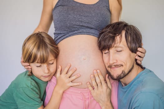 Father and elder son listen to mom's pregnant belly.
