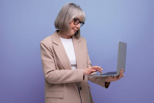 close-up of a confident 60s middle-aged woman in a jacket with a laptop on a bright background with copy space