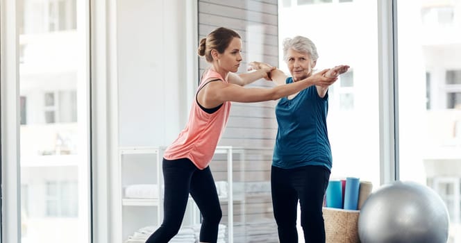 Staying fit helps prevent disease and chronic conditions. a fitness instructor helping a senior woman during a yoga class.