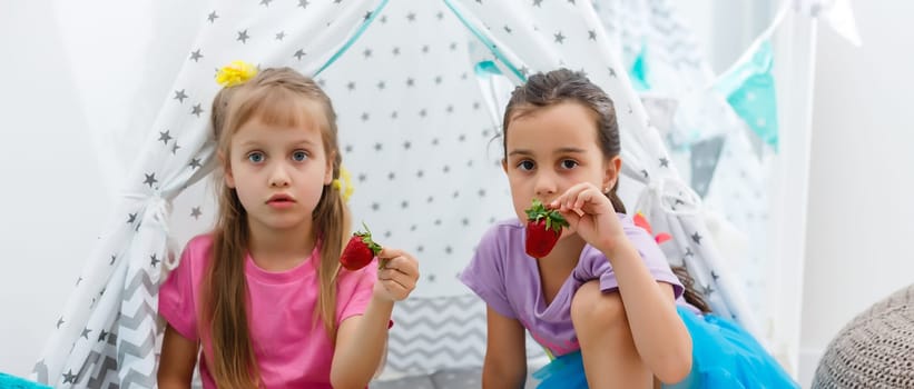 Two little cute girls sitting and eating strawberries