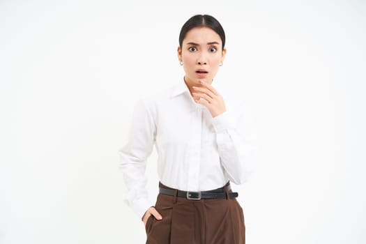 Asian saleswoman with shocked face, opens mouth and stares at camera, stands over white background