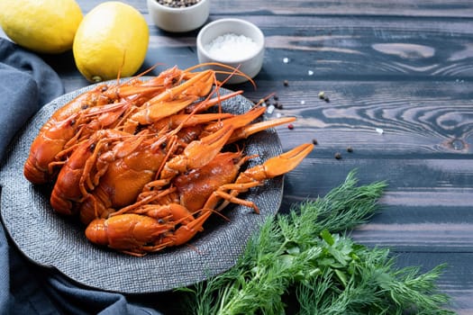 cooked crawfish on black plate with lemons and spices on wooden background