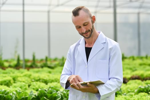Smiling male researcher, geneticist, biologist inspecting vegetable, working in an experimental greenhouse