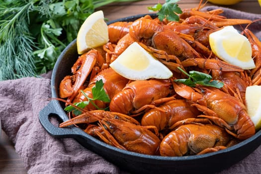 cooked crawfish in black saucepan with lemons and spices on wooden background