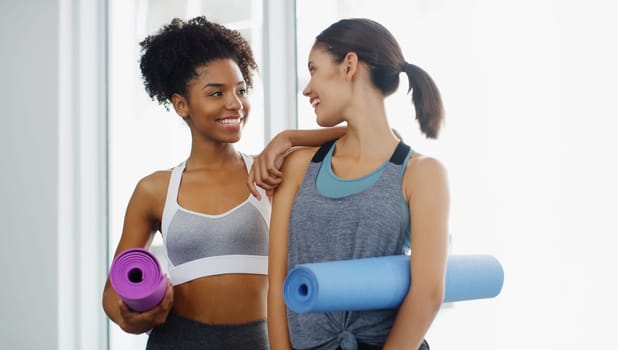 Well be yoga buddies forever. two attractive young women standing and holding yoga mats and posing before working out indoors
