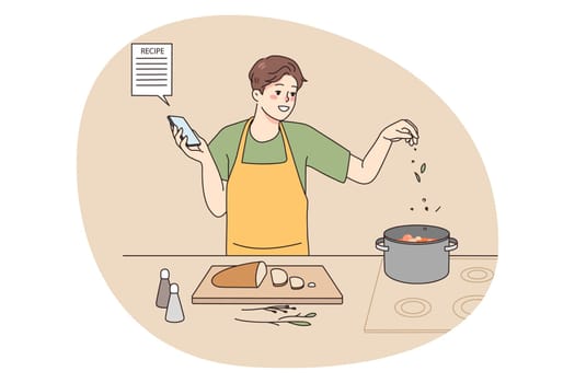 Smiling man cooking with recipe on cellphone