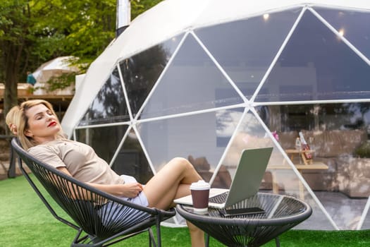 Positive woman chatting on laptop and and looking at screen near dome geometric structure