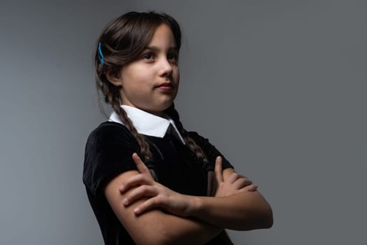 Portrait of little girl with Wednesday Addams costume during Halloween. Serious expression and dark atmosphere with dark background.