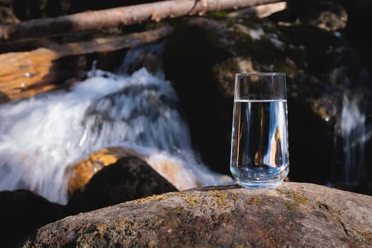 Pure water in a transparent glass against the backdrop of a mountain river in the background. Healthy food and clean natural water