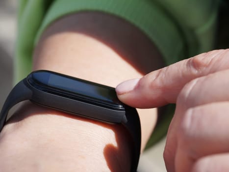 Using a fitness bracelet, a woman presses her finger on the display of a fitness bracelet