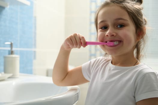 Close-up lovely child girl brushing teeth, smiling with beautiful smile looking at camera. Dental health and oral hygiene.