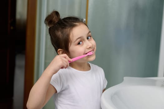 Dental care and oral hygiene for healthy white baby teeth. Close-up smiling child girl brushing teeth looking at camera.