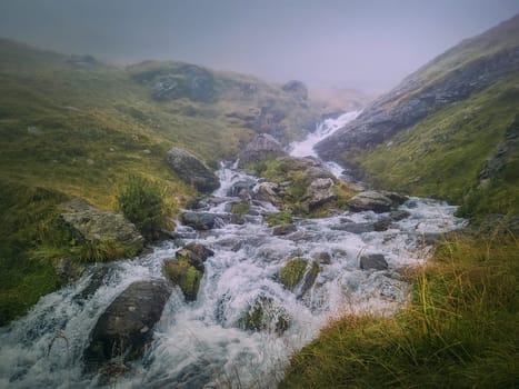 Fast stream flowing across a rocky valley in Fagaras Mountains. River with waterfalls and dense mist landscape