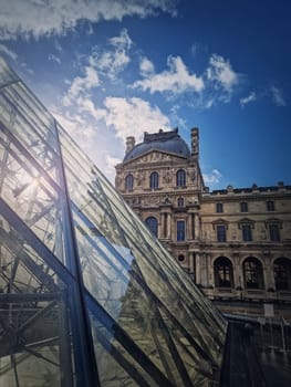 Outdoors view to the Louvre Museum in Paris, France. Vertical shot of the historical palace building with the modern glass pyramid in front