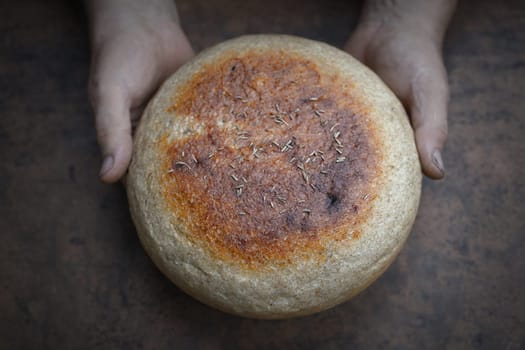 Homemade crusty loave of bread on wooden background. Baker holding fresh bread in the hands. view from above. Dark mood