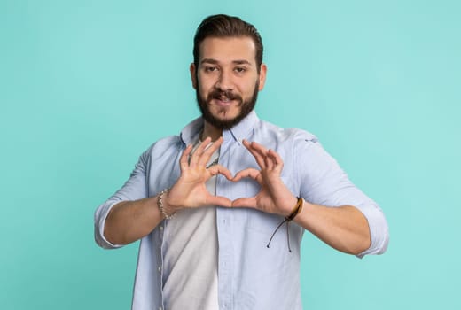 Smiling arabian man makes heart gesture demonstrates love sign expresses good feelings and sympathy