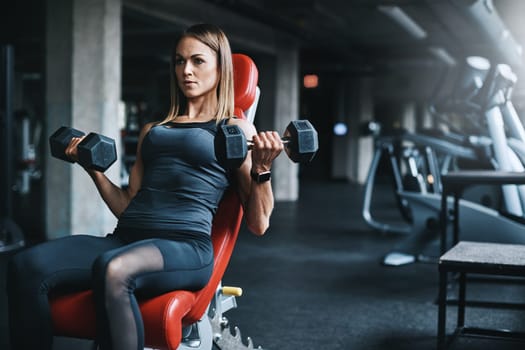 Where strong bodies are sculpted. a young woman working out with weights in a gym.