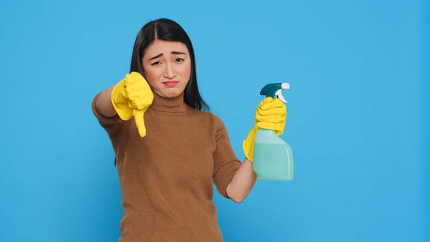 Upset unhappy housekeeper holding hygiene detergent spray doing disapproval sign