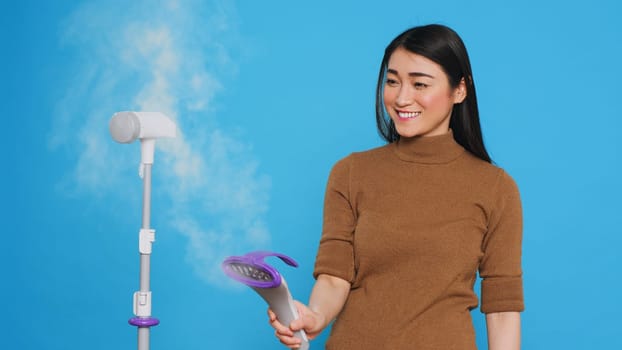Smiling cleaning lady using steamer to ironing clothes in studio