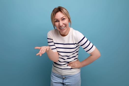 optimistic adorable happy blonde girl in casual outfit speaks emotionally on blue studio background with copy space